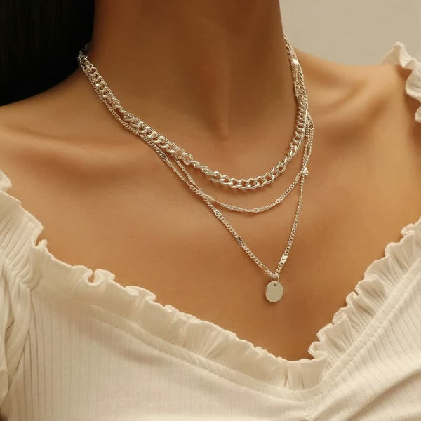 Zilveren ketting met meerdere lagen en ronde hanger, gedragen door vrouw in witte blouse. Trendy sieraden, modieuze accessoires, elegante stijl.