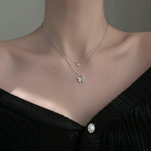 Zilveren vlinderketting op vrouwelijk model, minimalistisch design, dubbele ketting, elegante sieraden, perfect voor modieuze accessoires.