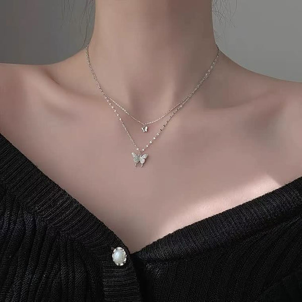 Zilveren vlinderketting met dubbele hanger, gedragen op een zwarte trui. Elegante damesaccessoire, perfect voor modieuze sieradenliefhebbers.