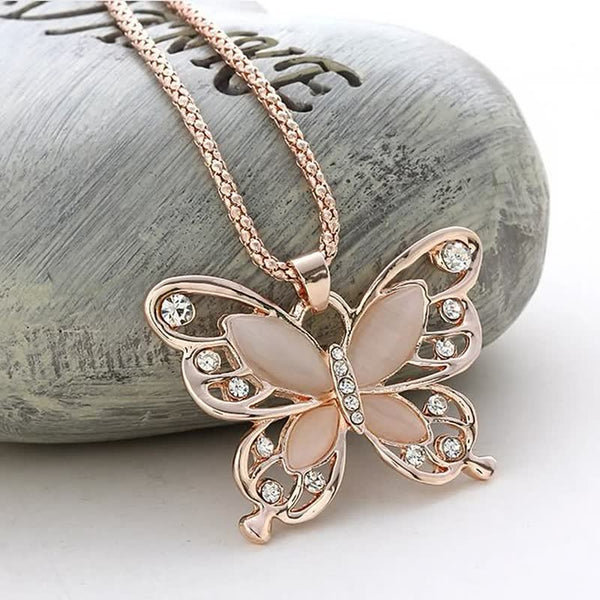 Gouden vlinderhanger met kristallen en roze accenten op een ketting, liggend op een grijze steen. Elegant sieraad, perfect voor damesmode.