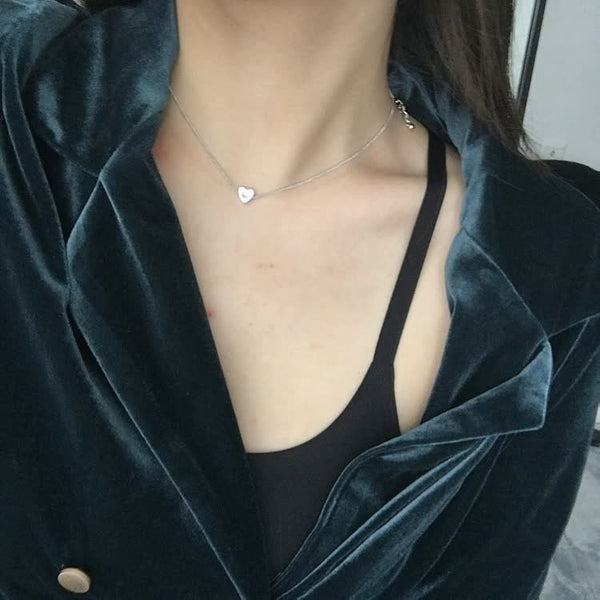 Vrouw in fluwelen blazer met hartvormige ketting, zwarte top zichtbaar. Modeaccessoires, elegante dameskleding, trendy sieraden.
