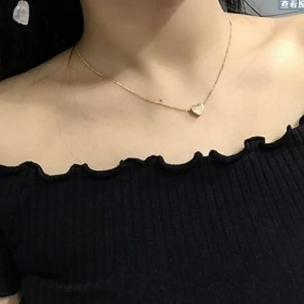 Vrouw met zwarte off-shoulder top draagt een delicate gouden ketting met hartvormige hanger. Elegante sieraden, minimalistische stijl.