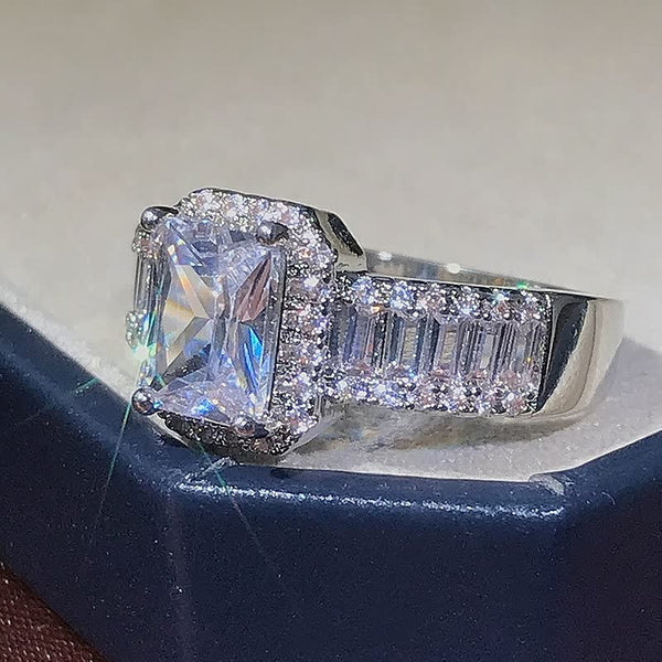 Verlovingsring met vierkante diamant, pavézetting en baguette geslepen zijstenen op zilveren band, sprankelend in licht.