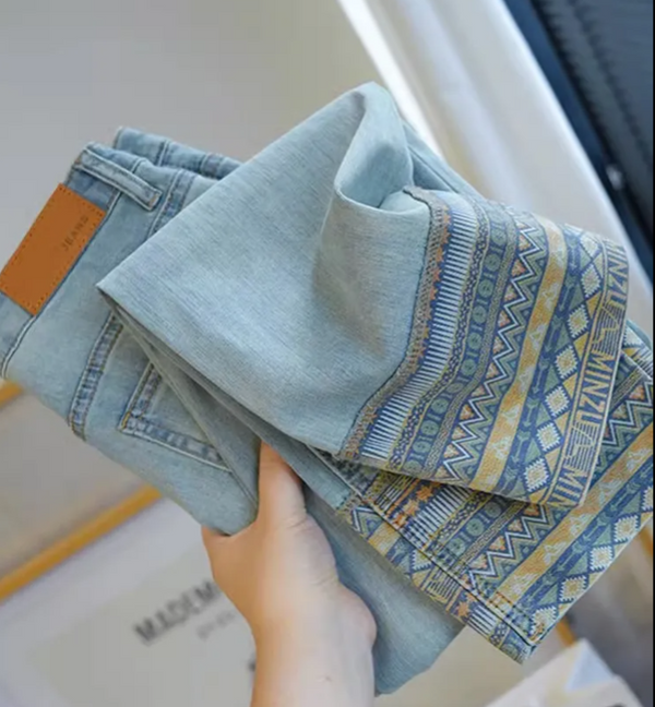 Hand houdt lichtblauwe jeans en sjaal met etnisch patroon vast. Modieuze kleding, denim broek, trendy accessoires, casual stijl.