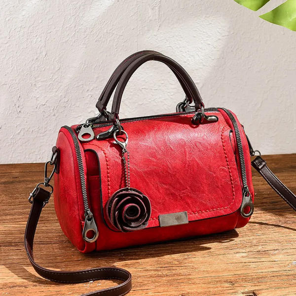 Rode leren handtas met rozenhanger, zilveren ritsen en verstelbare schouderriem op houten tafel. Stijlvolle damesaccessoire voor dagelijks gebruik.