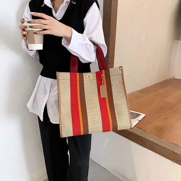 Vrouw met zwart-witte outfit houdt een koffiebeker en draagt een gestreepte handtas in beige, rood en oranje tinten. Stijlvolle modeaccessoire.
