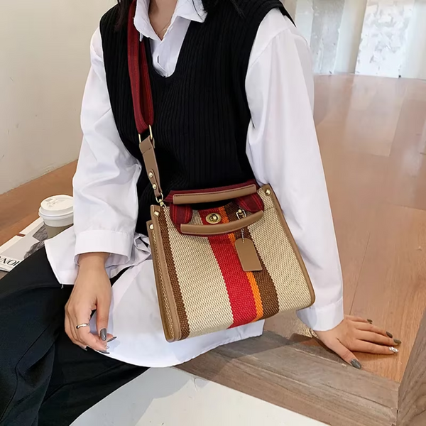 Stijlvolle handtas met rood, bruin en beige strepen, gedragen door vrouw in witte blouse en zwarte trui. Modieuze accessoire voor dames.