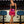 Vrouw in zwarte top en roze paillettenrok met veren, poseert in moderne bar met blauwe barkrukken en neonverlichting. Fashion, avondkleding, trendy outfit.
