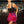 Vrouw in bar met zwarte top en roze paillettenrok met veren, omringd door glazen en flessen. Party outfit, avondkleding, modetrends.