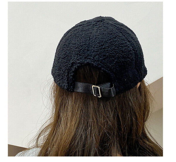 Zwarte fleece pet met verstelbare riem, gedragen door persoon met lang bruin haar. Stijlvolle winteraccessoire, unisex design.