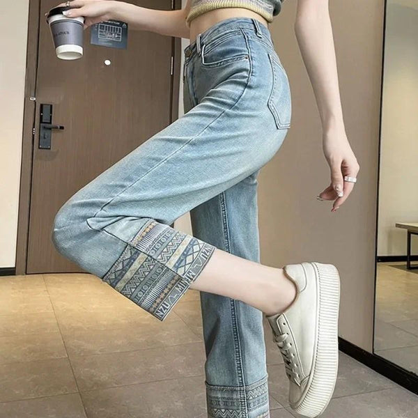 Vrouw in trendy blauwe jeans met etnische print en witte sneakers, houdt een koffiebeker vast. Modieuze casual outfit, perfect voor dagelijks gebruik.
