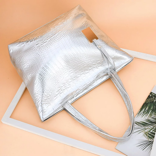 Zilveren krokodillenleren handtas op beige achtergrond, stijlvolle damesaccessoire met lange hengsels, modetrend 2023, luxe tas voor dagelijks gebruik.