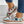 Vrouw draagt kleurrijke bloemen sneakers met witte veters en kurkzool, gecombineerd met blauwe jeans. Trendy damesmode, casual schoenen.