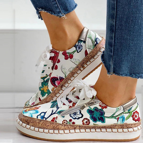 Vrouw draagt kleurrijke bloemen sneakers met witte veters en kurkzool, gecombineerd met blauwe jeans. Trendy damesmode, casual schoenen.