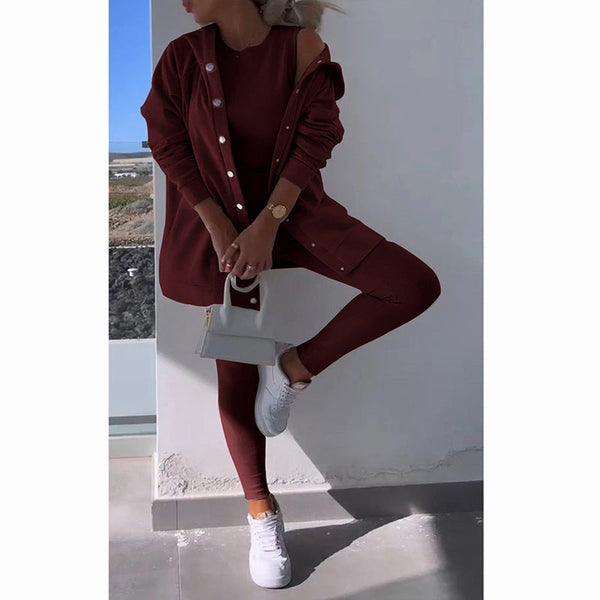 Vrouw in bordeauxrode outfit met legging en oversized jas, witte sneakers en handtas. Stijlvolle mode, casual chic, moderne dameskleding.