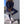 Vrouw in donkerblauwe sportoutfit met witte sneakers en handtas, poseert tegen een muur. Modieuze sportkleding, casual stijl, trendy accessoires.