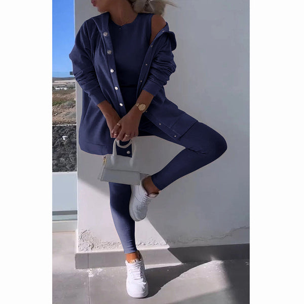 Vrouw in donkerblauwe sportoutfit met witte sneakers en handtas, poseert tegen een muur. Modieuze sportkleding, casual stijl, trendy accessoires.