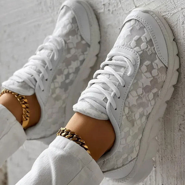Witte sneakers met bloemenpatroon en gouden enkelband, gedragen door een persoon in witte broek. Stijlvolle damesmode, trendy schoenen.