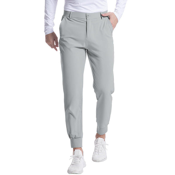 Man in grijze sportbroek en witte sneakers, staand op witte achtergrond. Comfortabele, stijlvolle activewear voor heren. Geschikt voor sport en casual.