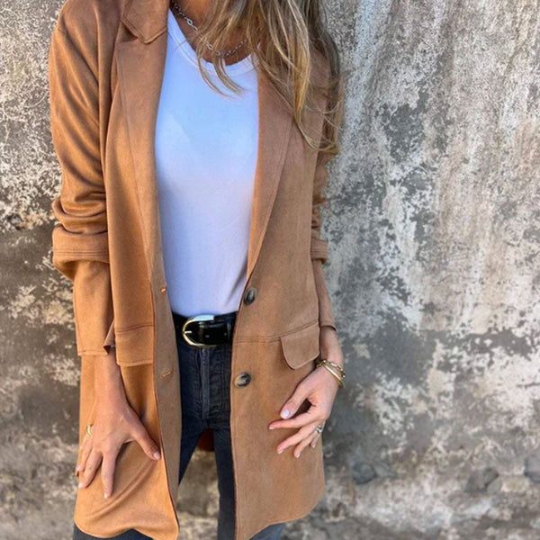 Vrouw in stijlvolle bruine suède jas, witte top en zwarte jeans tegen een verweerde muur. Modieuze herfstoutfit, casual chic stijl.