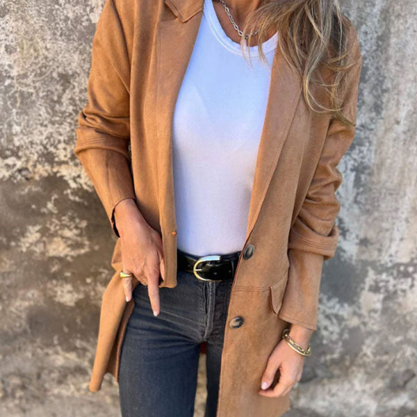 Vrouw in bruine suède jas, witte top en zwarte jeans tegen betonnen muur. Modieuze herfstkleding, casual damesoutfit, trendy jasstijl.