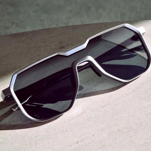Zilveren zonnebril met geometrisch ontwerp en donkere glazen op een betonnen oppervlak. Moderne unisex zonnebril, stijlvol en trendy accessoire.