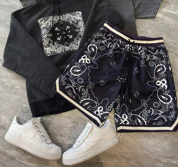 Zwarte hoodie en korte broek met paisley-patroon, gecombineerd met witte sneakers. Streetwear outfit, casual mode, trendy kledingstijl.
