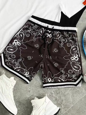 Zwart-witte sportshorts met paisley-patroon, naast witte sneakers, een tennisracket en honkbal, op een grijze achtergrond. Perfect voor sportieve activiteiten.