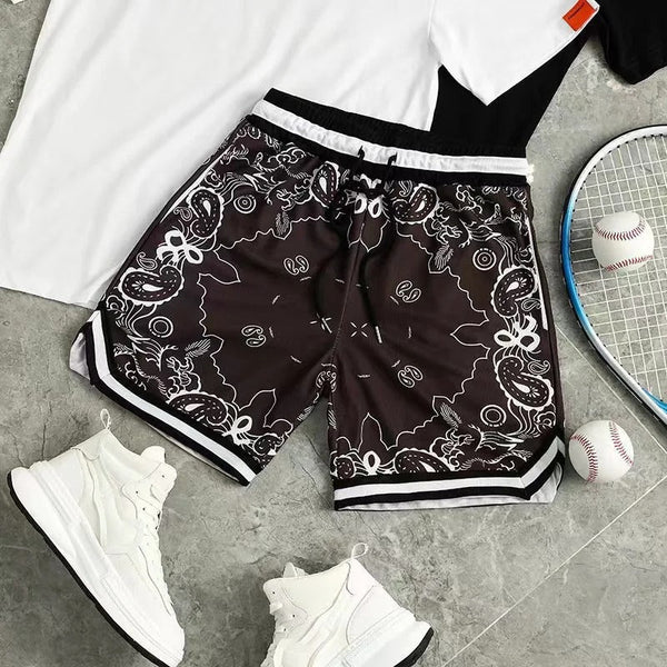 Zwart-witte sportshorts met paisley-patroon, naast witte sneakers, een tennisracket en honkbal, op een grijze achtergrond. Perfect voor sportieve activiteiten.