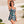 Vrouw in blauwe bloemenbadpak, strandachtergrond, zomermode, tropische print, stijlvolle zwemkleding, strandkleding, vakantieoutfit.