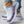 Witte en paarse gebreide sneakers met dikke zool, gedragen door persoon met gouden enkelbanden en blauwe jeans. Comfortabele damesmode schoenen.