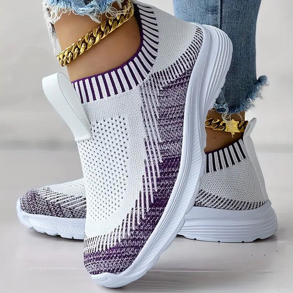 Witte en paarse gebreide sneakers met dikke zool, gedragen door persoon met gouden enkelbanden en blauwe jeans. Comfortabele damesmode schoenen.