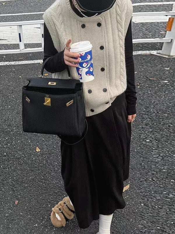 Vrouw in stijlvolle herfstoutfit met beige kabeltrui, zwarte rok en tas, houdt een koffiebeker vast. Modieuze straatstijl, casual chic look.