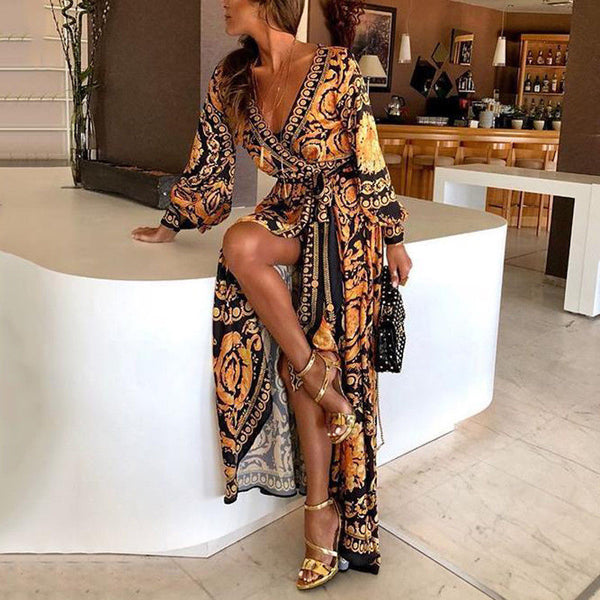 Vrouw in elegante wikkeljurk met barokprint, V-hals en split, zittend op witte tafel. Perfecte zomerjurk voor dames, modieuze outfit.